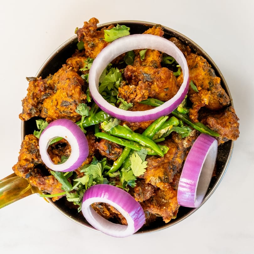 Desi Chichas' Indian chicken pakora, garnished with red onion rings, green chilies, and cilantro.