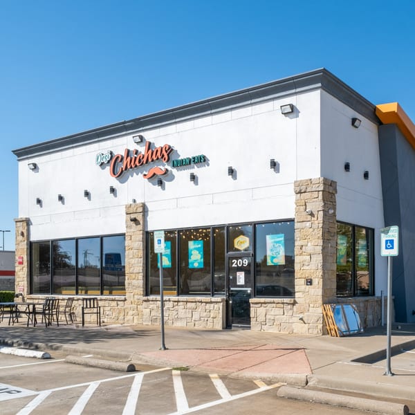 Exterior of Desi Chichas Indian Eats restaurant with outdoor seating and a clear blue sky.