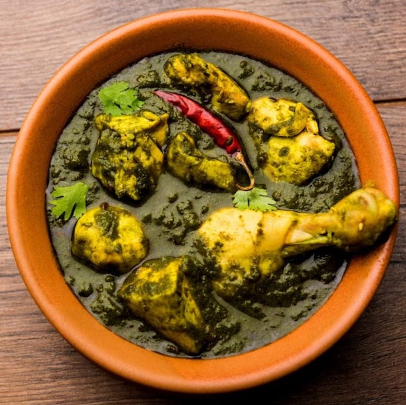 Indian Palak Chicken, a green spinach curry with chicken pieces, garnished with cilantro and a red chili.