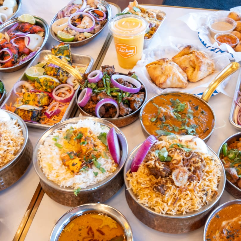 A table laden with various Indian dishes from Desi Chichas, including curries, biryani, and grilled items.