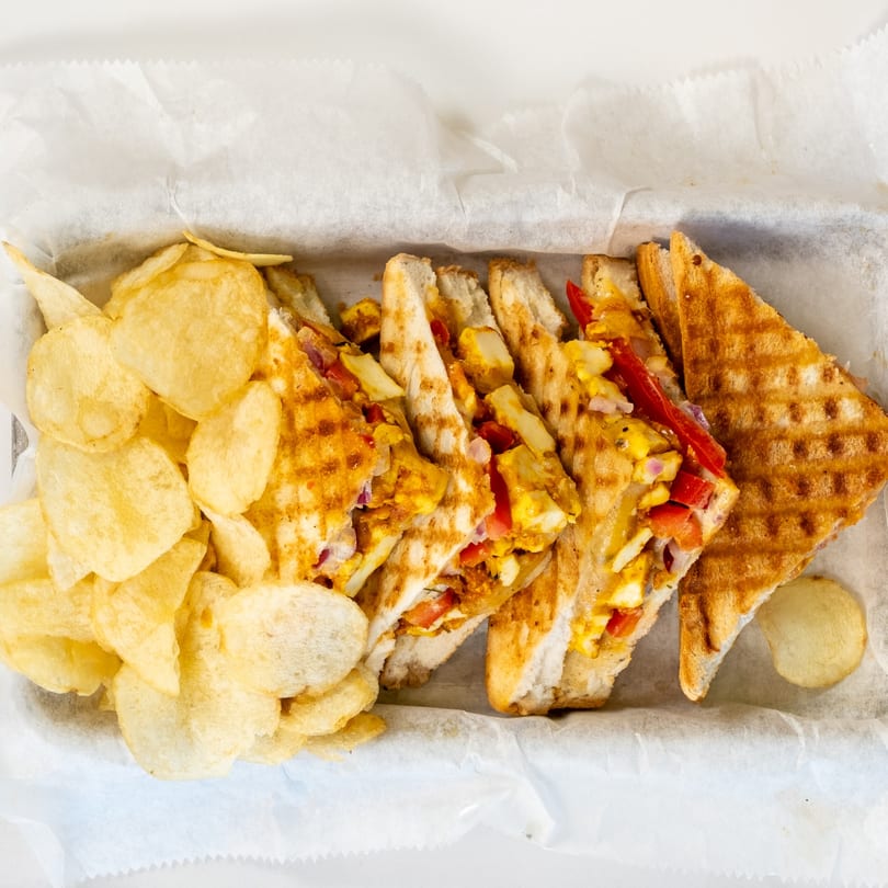 Grilled Indian sandwiches with paneer, peppers, and onions, served with potato chips in a basket.