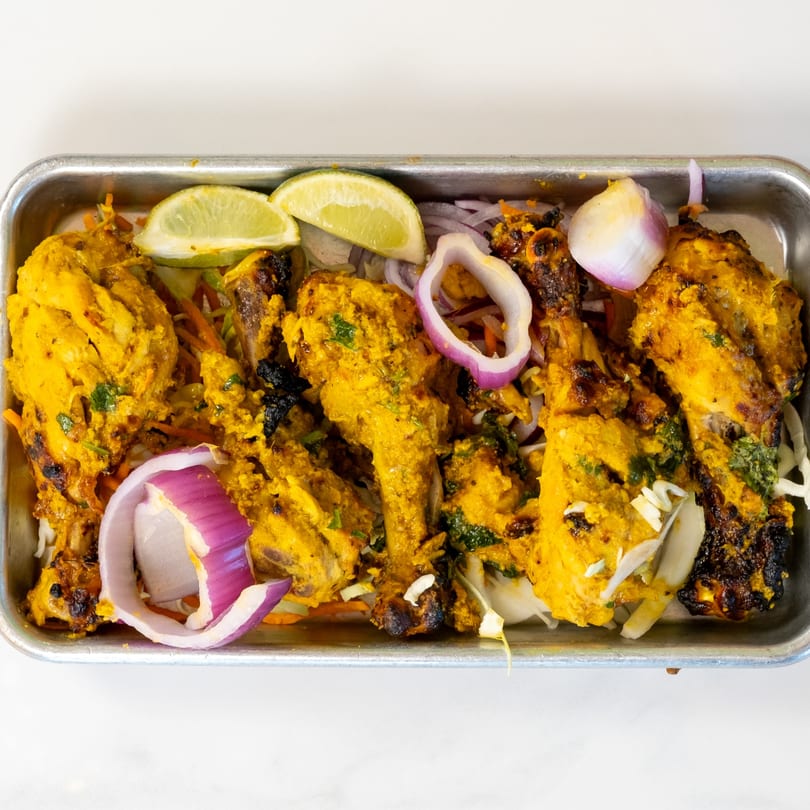 Indian tandoori chicken drumsticks with lime wedges and red onion in a metal tray.