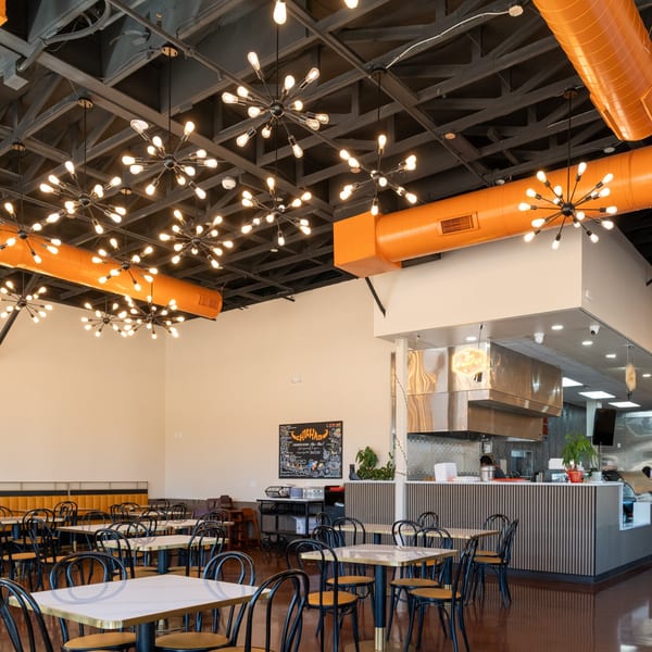 Interior of Desi Chichas Indian restaurant with modern starburst chandeliers, orange ductwork, and empty tables.