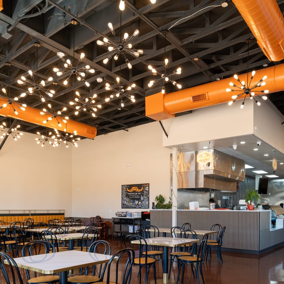 Interior of Desi Chichas Indian restaurant with modern starburst chandeliers, orange ductwork, and empty tables.
