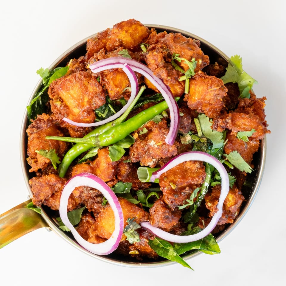 Desi Chichas' Chicken 65, a vibrant Indian dish with fried chicken, red onions, green chilies, and cilantro.
