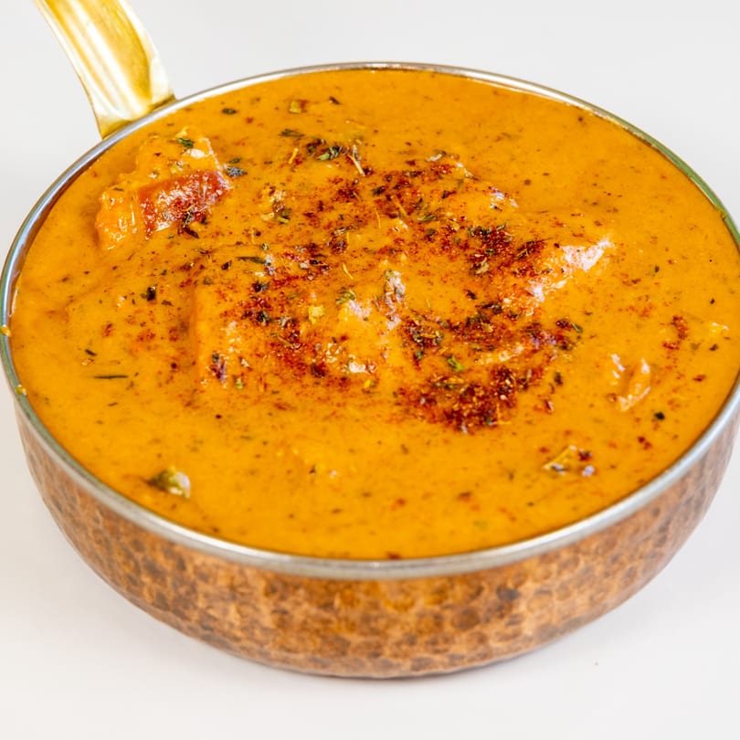 Desi Chichas' Indian butter chicken curry, garnished with herbs and spices, in a copper serving pot.